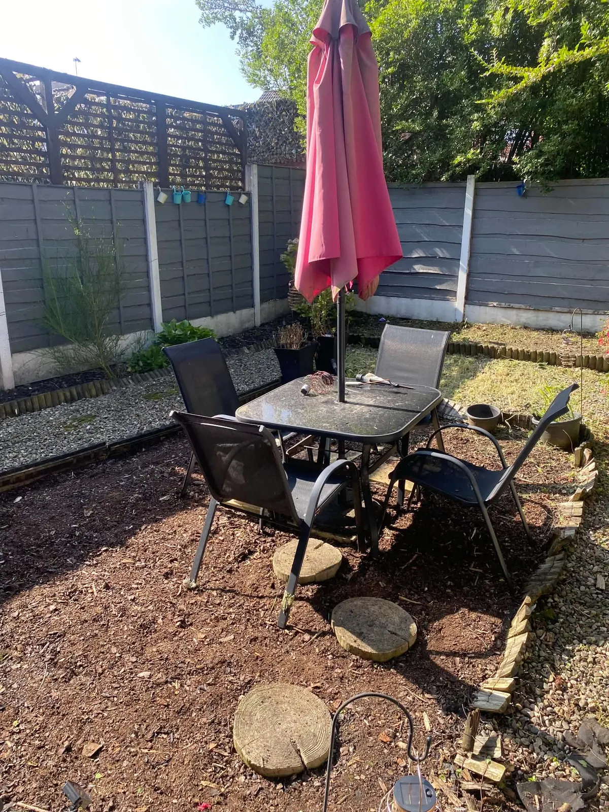 Garden table and chairs on a cleared bark bed with a gravel border beside a fence