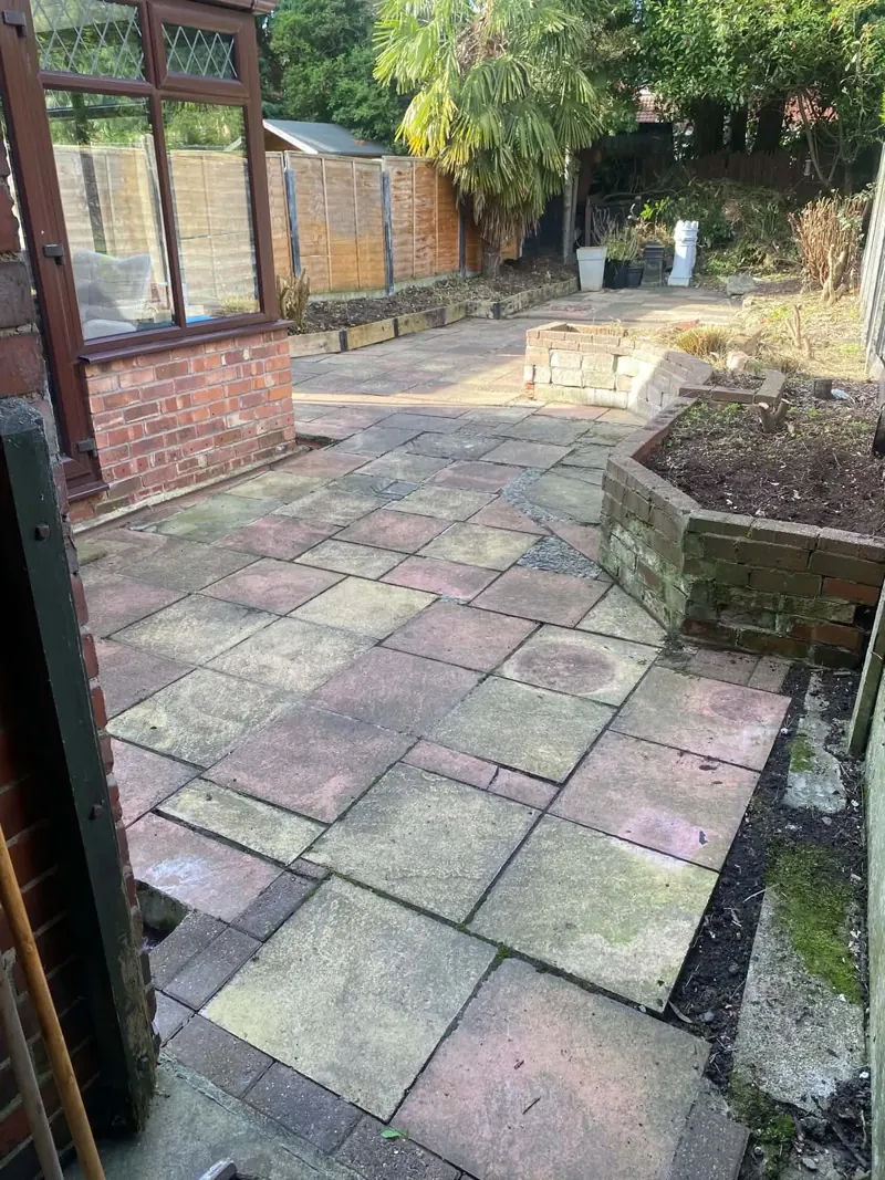 Cleared patio and raised brick bed beside a conservatory in a Bredbury garden, with weathered green slabs at the edge