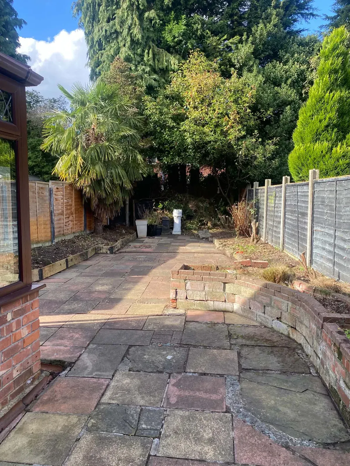 Cleared paved patio and curved raised brick bed beside a conservatory after the Bredbury garden clearance, with a fence and trees beyond