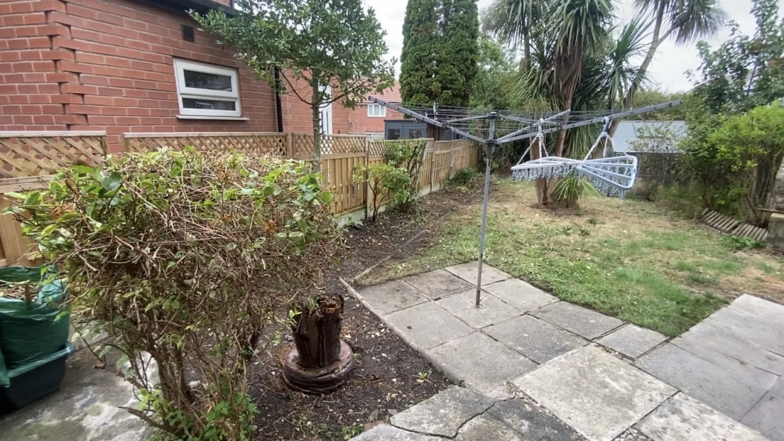Cleared back garden with a rotary washing line, bare border soil, a tree stump and a lawn beside a paved patio