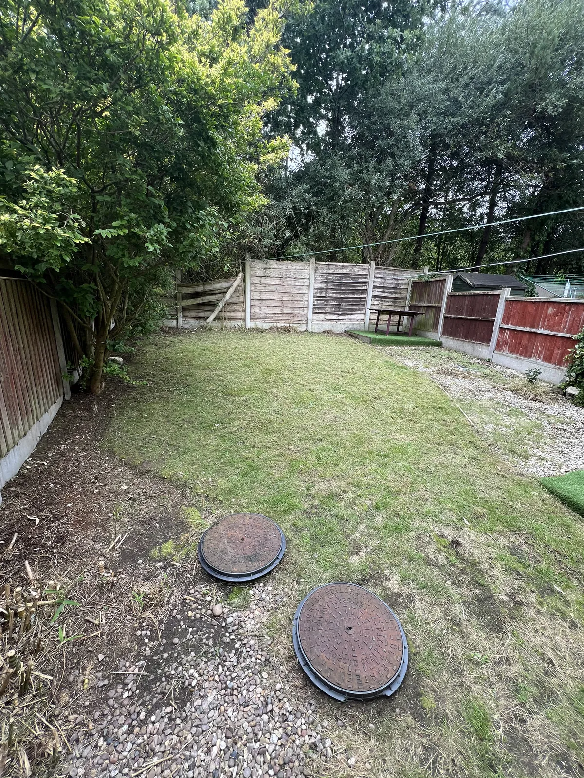 Back garden lawn cut short with tidy edges against a gravel strip, fences behind and two round inspection covers lying on the ground at the front