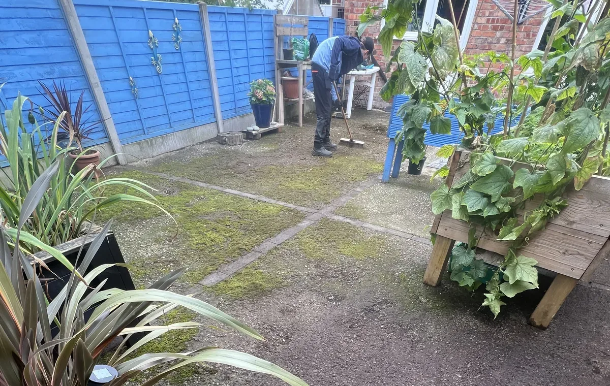 Terrace back yard being swept and cleared, with mossy flags, pots and a blue fence