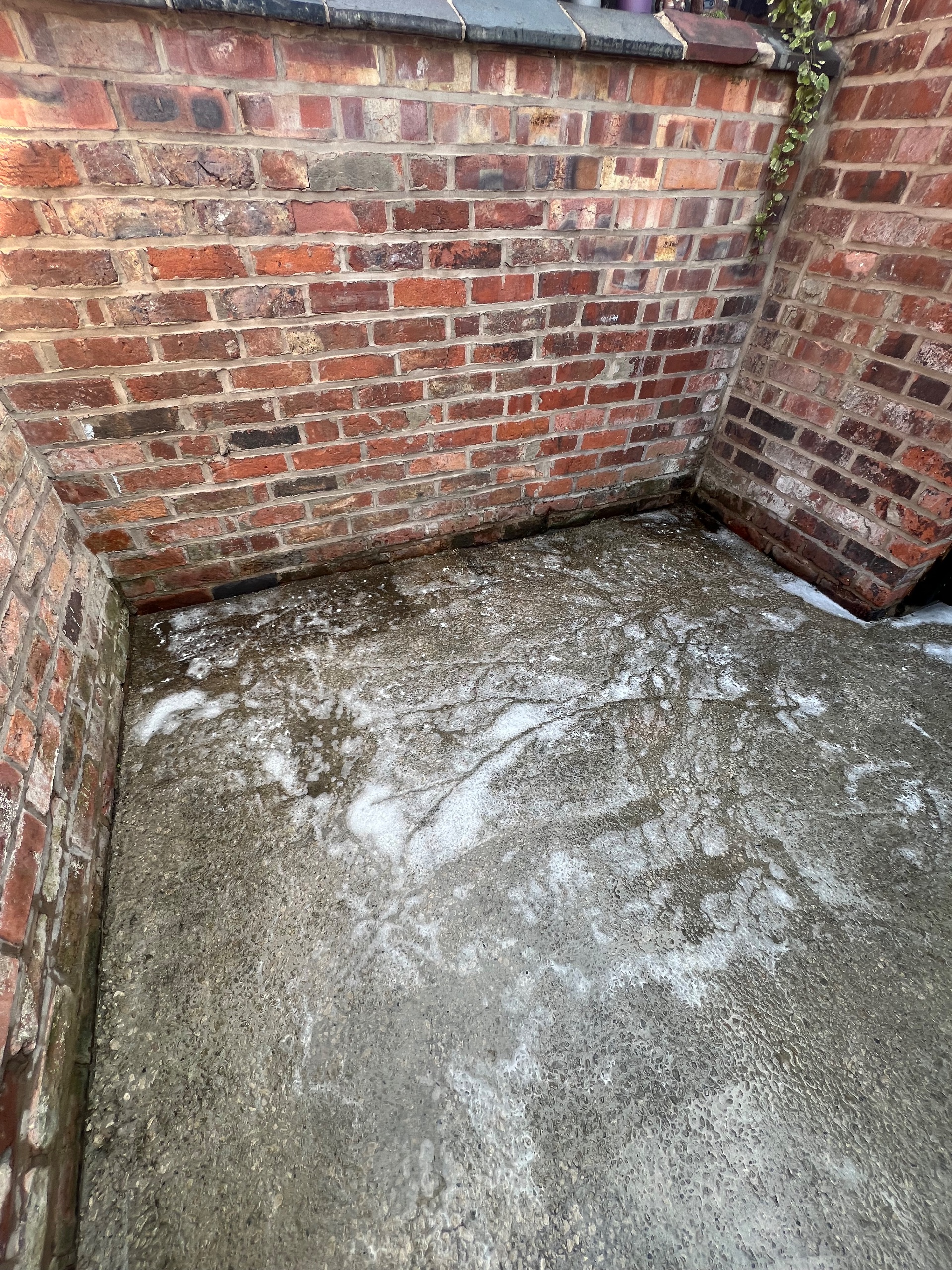 concrete yard with detergent suds after pressure washing against brick walls